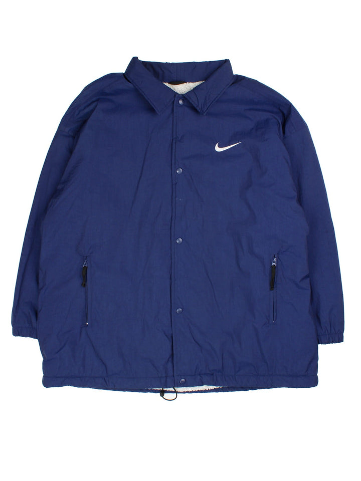 Nike Coach Jacket in a blue colourway. Fleece lining with full button up front, double zip pocket with small classic nike swoosh. Large Nike logo across the back.