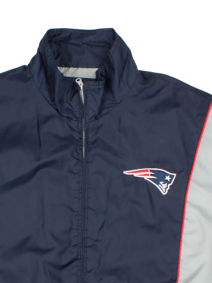 New England Patriots NFL Windbreaker Jacket in a blue colourway with grey panelling. Full zip up, multiple pockets, small logo on the front and large text logo across the back.