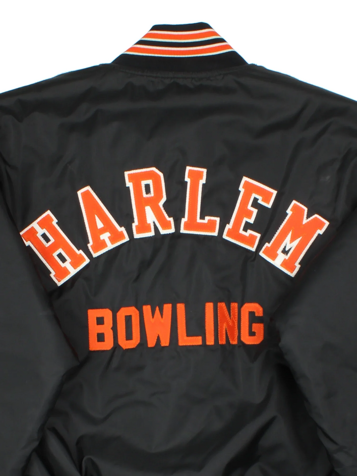 Vintage Harlem Bowling Team Varsity Jacket in a black colourway with orange detailing. Full button up front, multiple pockets and small logo on the front. Large team logo across the back.