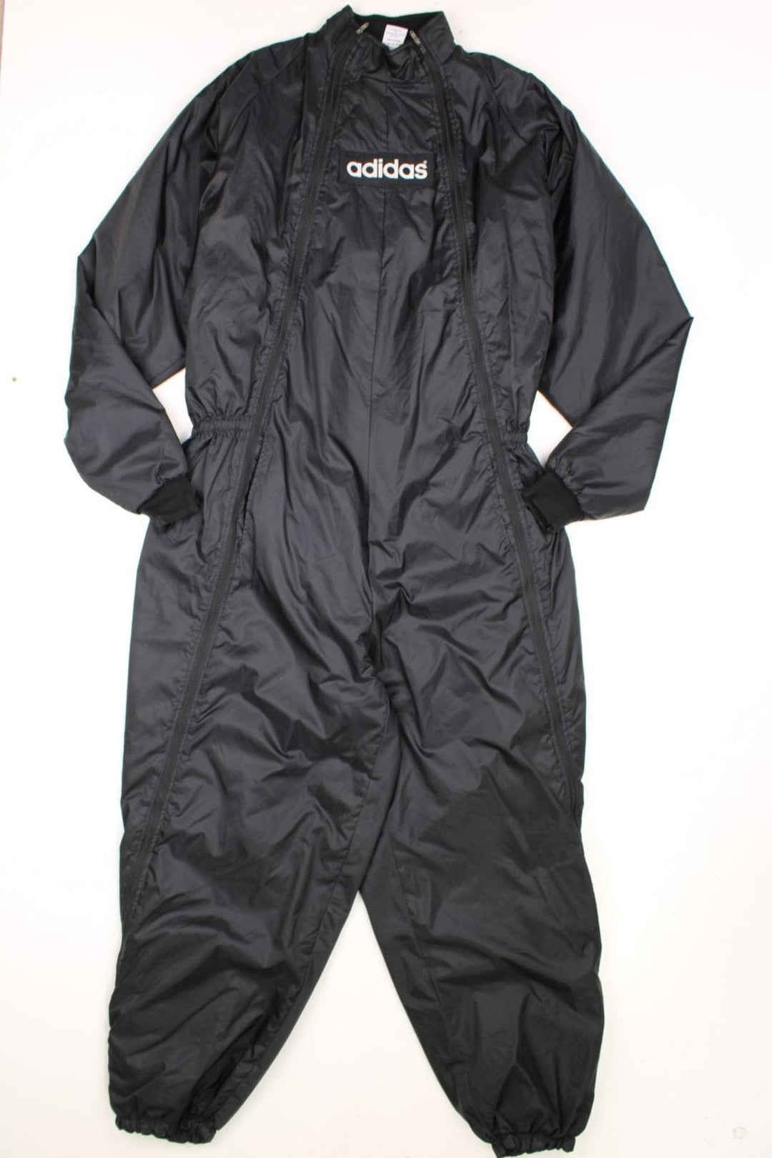 Adidas Jumpsuit in a black colourway, full zip down with side pockets, quilted lining, and has the spell out logo embroidered across the front and back. 