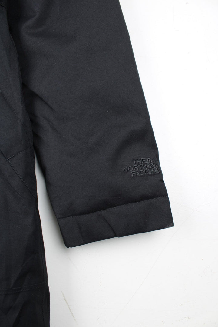 The North Face Jacket in a black colourway. Zips up and has side pockets, insulated lining, hooded with a faux fur trim, and has the logos embroidered on the left sleeve.