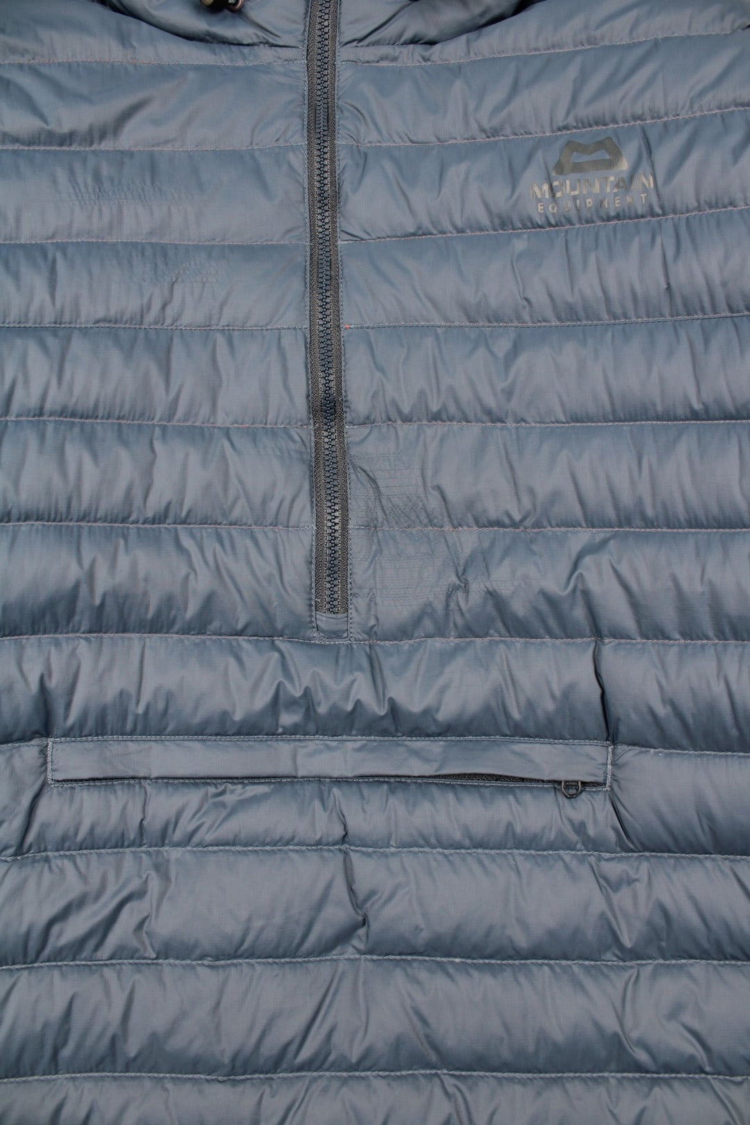 Mountain Equipment Earthrise Down Jacket in a blue colourway. Half zip pullover jacket, has two front pouch pockets, insulated lining, hooded, and has the logo printed on the front.