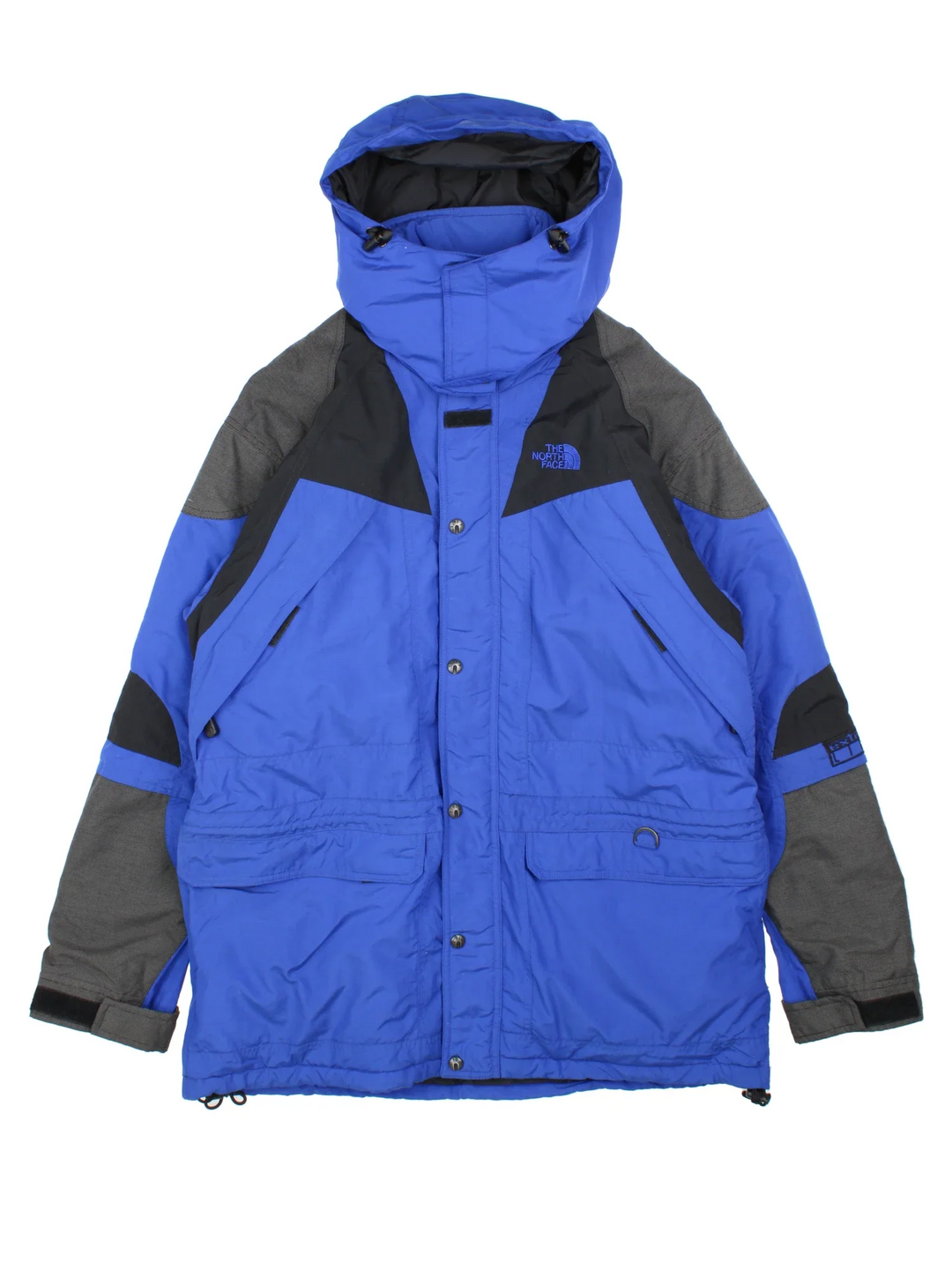 The North Face Coat in a blue colourway with black panelling, full zip up and button up. multiple pockets and has the logo embroidered on the sleeve and front.