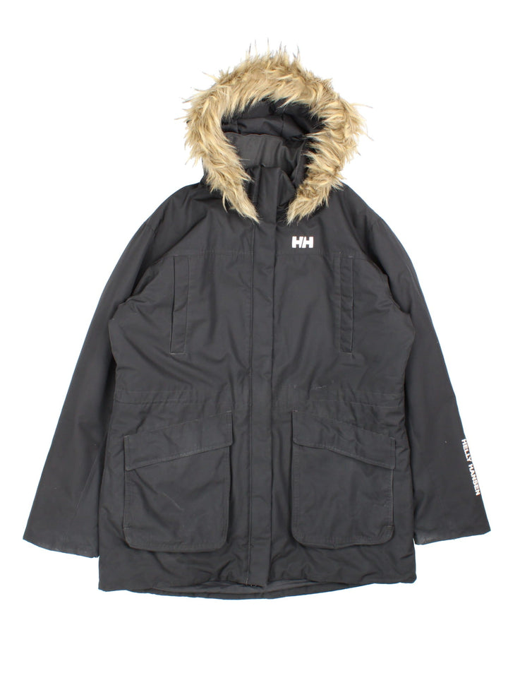 Helly Hansen Parka Coat in a black colourway. Multiple pockets on front and has a faux fur parka hood and the logo on the front.