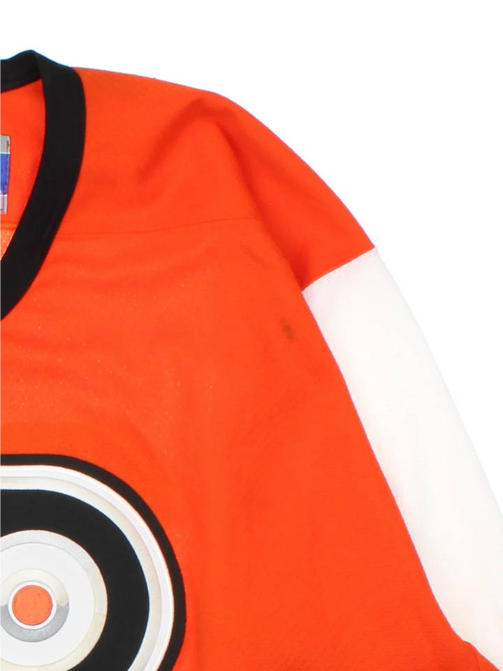 Philadelphia Flyers NHL Jersey in a  orange colourway, features embroidered logos and badge on the front with black and white stripe detailing on the sleeves and hem.