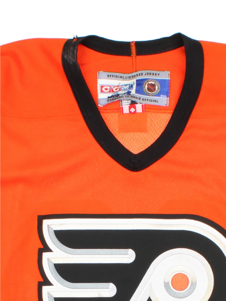 Philadelphia Flyers NHL Jersey in a  orange colourway, features embroidered logos and badge on the front with black and white stripe detailing on the sleeves and hem.