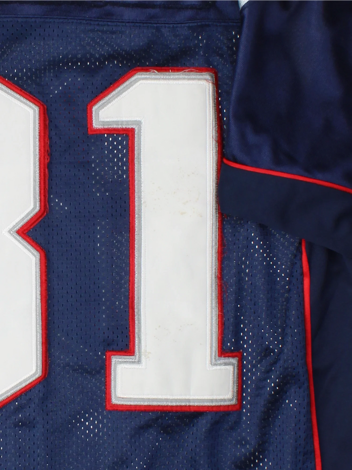 New England Patriots Reebok NFL Jersey in the blue home kit colourway with silver and red detailing, features embroidered logos and badge on the front and player name MOSS #81 on the back.