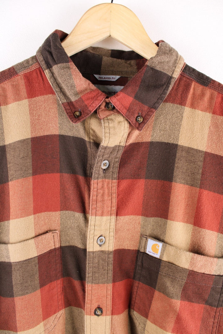 Carhartt button-down shirt in brown, red, and tan check, with two breast pockets and a small logo patch on the chest.