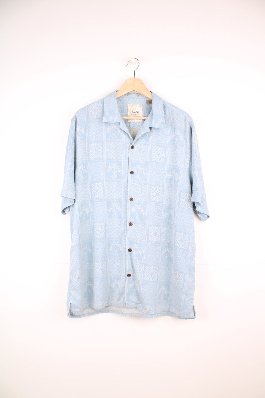 Pale blue hawaiian shirt by Tasso Elba, featuring tropical patterns and palm tree motifs in white, and brown wooden buttons.  