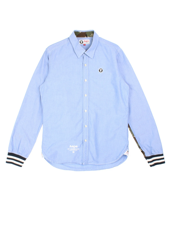 A Bathing Ape By Bape Oxford Shirt in a blue colourway and has camo panelling by on the sleeves, button up with the logo embroidered on the front.