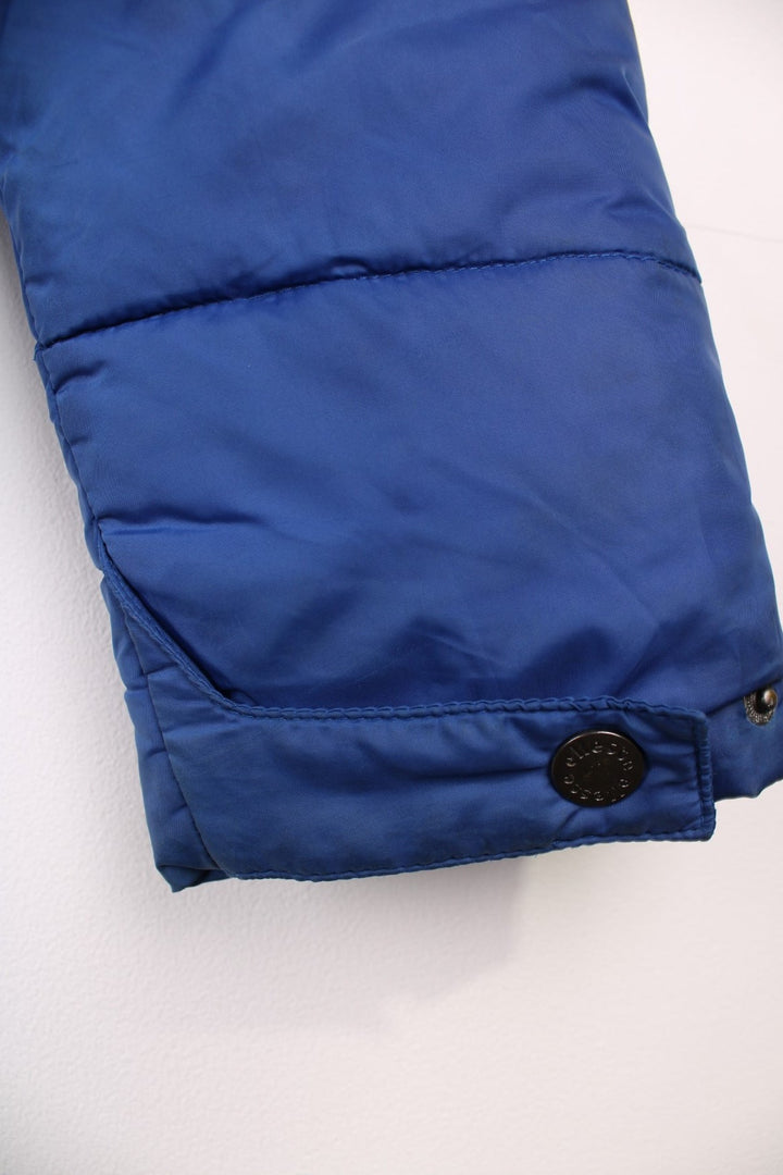 Y2K Ellesse Coat in a blue colourway, the coat has a faux fur trim hood, is filled with a polyester filling and has two hand warmer pockets on the front panels. There is an Ellesse Ski patch sewn onto the front and Ellesse embroidered on the sleeve. 