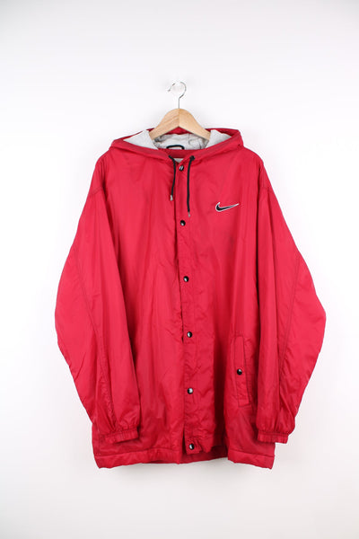 Red Nike coat with popper fastenings. Features embroidered logo on the chest and back. 