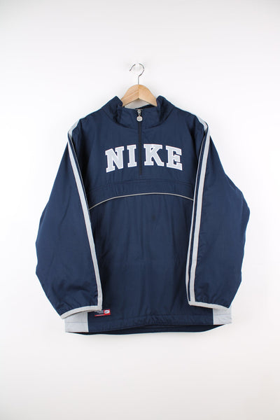 Blue and grey Nike pullover coat with quarter zip. Features embroidered spell out logo across the chest, stripe detail on each sleeve and large pouch pocket.
