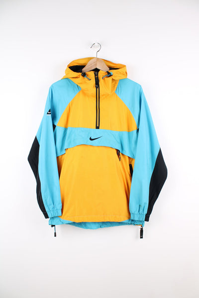 Nike ACG blue, yellow and black pullover packable windbreaker jacket with half zip. Features embroidered logo and pouch pocket.