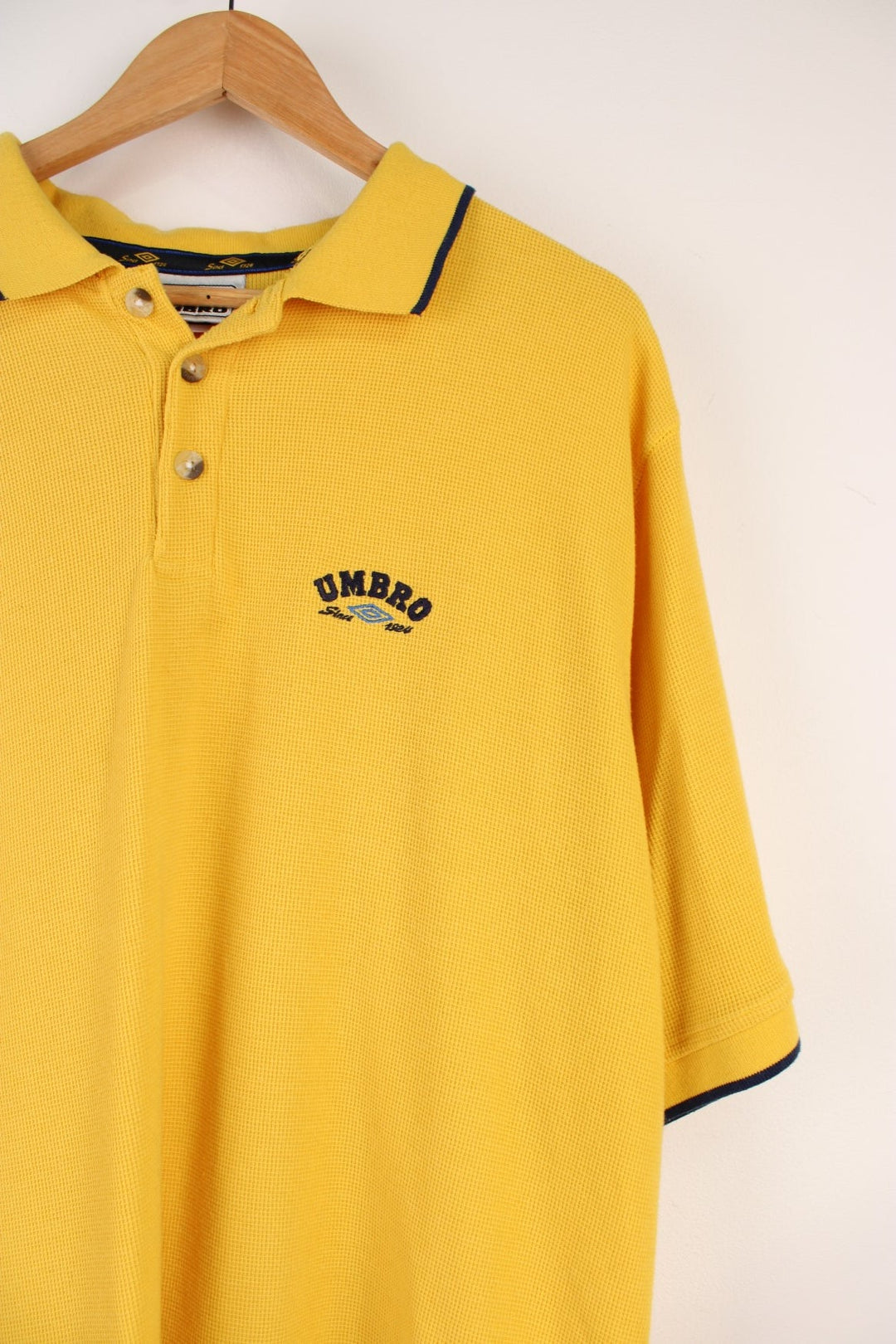 Umbro Polo Shirt in a yellow colourway with navy stripes going round the end of the cuffs and collar, button up, and has the logo embroidered on the front.