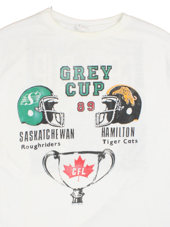 Vintage 1989 CFL Grey Cup Saskatchewan Roughriders vs Hamilton Tiger Cats tee in white with helmet face-off graphic on the front and photo of trophy on the back.