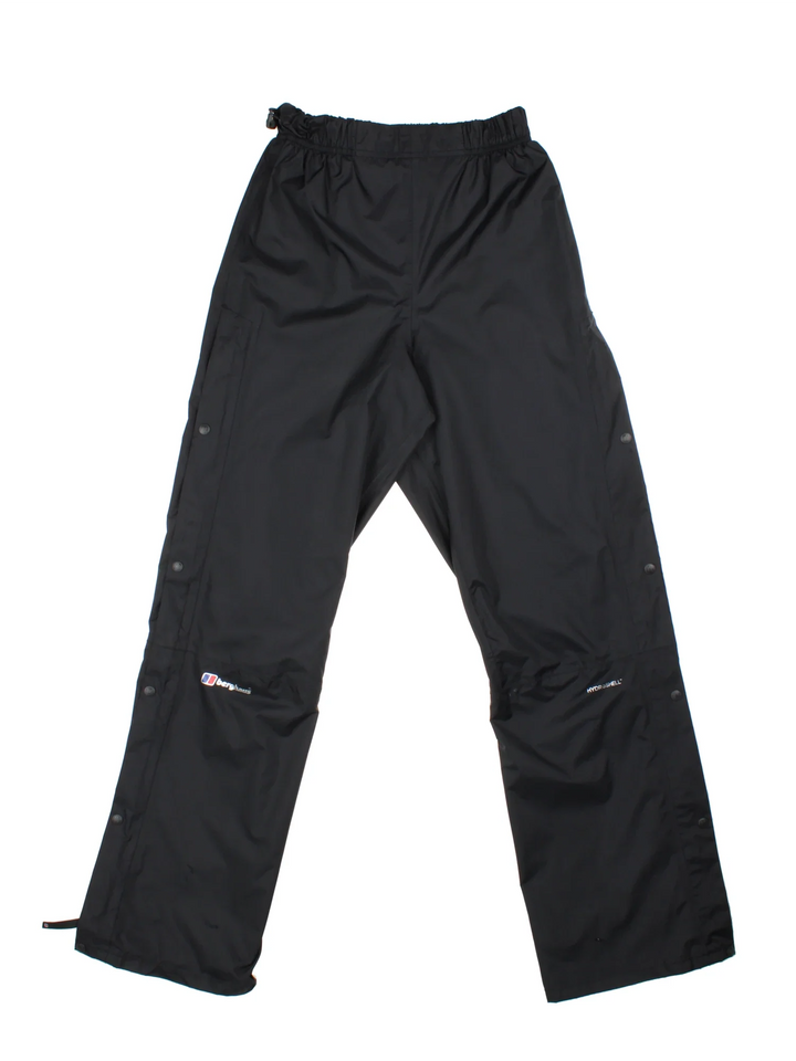 Berghaus Hydroshell Hike Trousers in a black colourway, does not have pockets, has an adjustable elasticated waist, popper button and zip down the side of the legs, and the logo printed on the front.