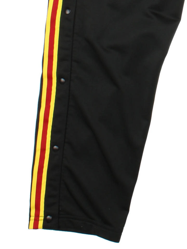 Reebok Popper Tracksuit Bottoms in a black colourway with yelow and red stripes going down the sides alongside popper button openings, has pockets, elasticated waist with drawstring, and the logo embroidered on the front.
