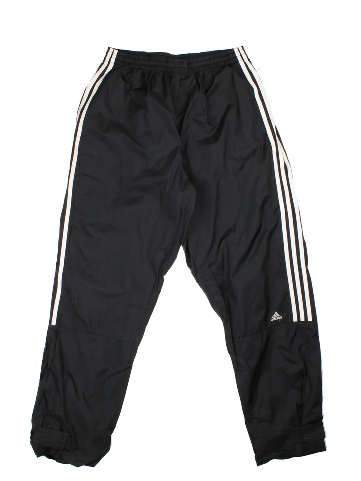 Vintage Adidas Tracksuit Bottoms in a black colourway with the iconic three stripes down the sides, has pockets, adjustable velcro straps by the cuffs, mesh lining, and the logo embroidered on the front.