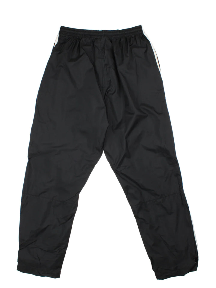 Vintage Adidas Tracksuit Bottoms in a black colourway with the iconic three stripes down the sides, has pockets, adjustable velcro straps by the cuffs, mesh lining, and the logo embroidered on the front.