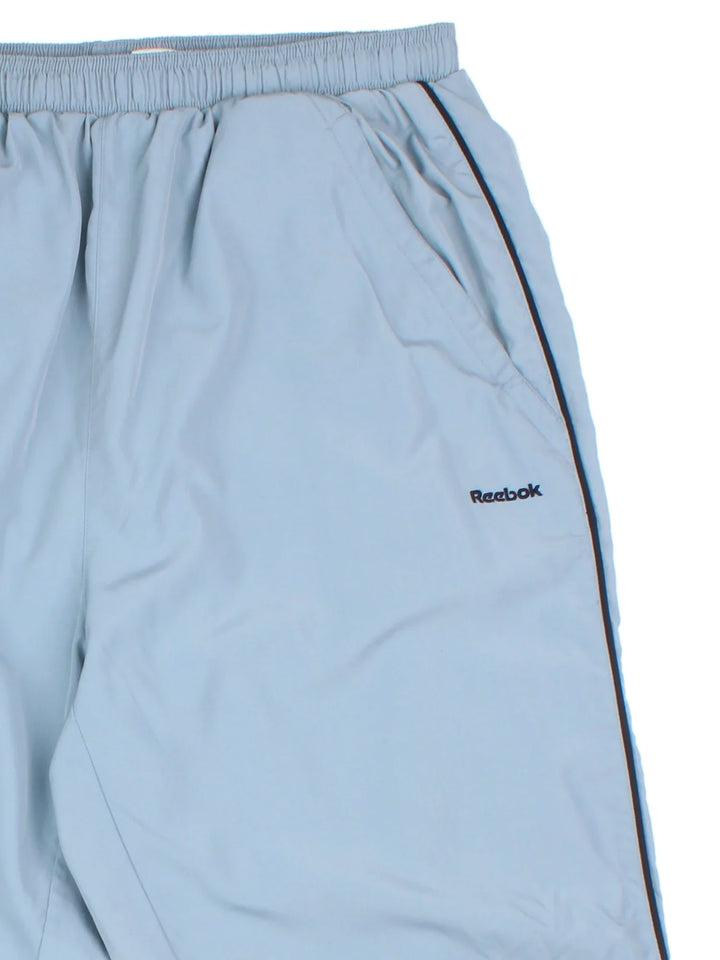 Reebok Tracksuit Bottoms in a blue colourway with stripes going down the sides, pockets, elasticated waist with drawstring, and the logo embroidered on the front and down the sides.