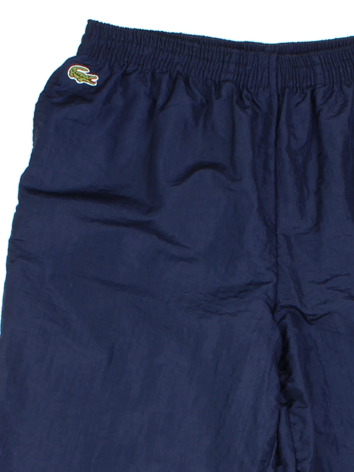 Vintage Lacoste Shell Pants in a blue colourway with pockets, elasticated waist with drawstring, cotton lining and the logo embroidered on the front.