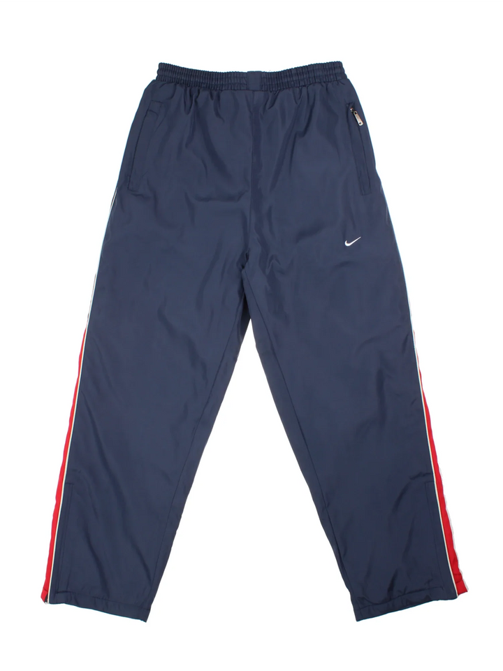 Nike Thermal Tracksuit Bottoms in a blue colourway with red and white panelling on the sides, has pockets, elasticated waist with drawstring, insulated thermal lining, and the swoosh logo embroidered on the front.