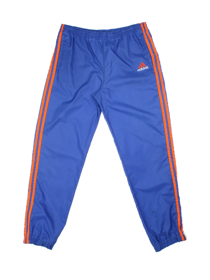 80's Adidas Shell Pants in a blue colourway with the iconic three stripes in orange down the sides, has side pockets, elasticated waist with drawstring, and the logo embroidered on the front.