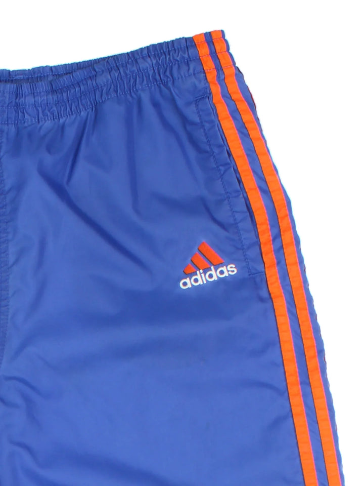 80's Adidas Shell Pants in a blue colourway with the iconic three stripes in orange down the sides, has side pockets, elasticated waist with drawstring, and the logo embroidered on the front.