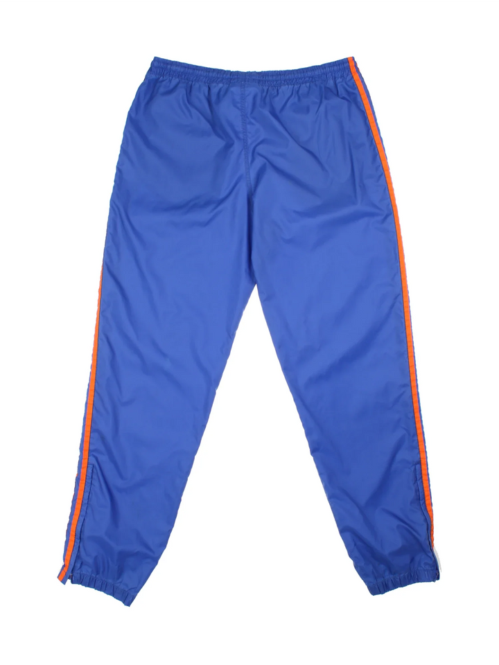 80's Adidas Shell Pants in a blue colourway with the iconic three stripes in orange down the sides, has side pockets, elasticated waist with drawstring, and the logo embroidered on the front.