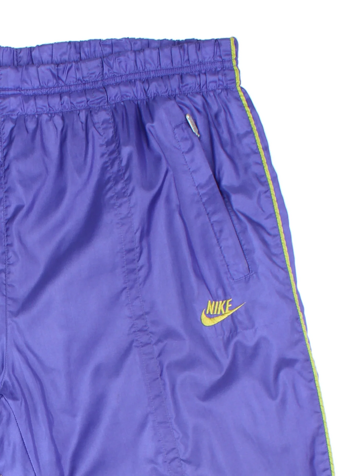 Vintage 80's Nike Shell Pants in a purple colourway with pockets, elasticated waist with drawstring, cotton blend lining, and the logo embroidered on the front.
