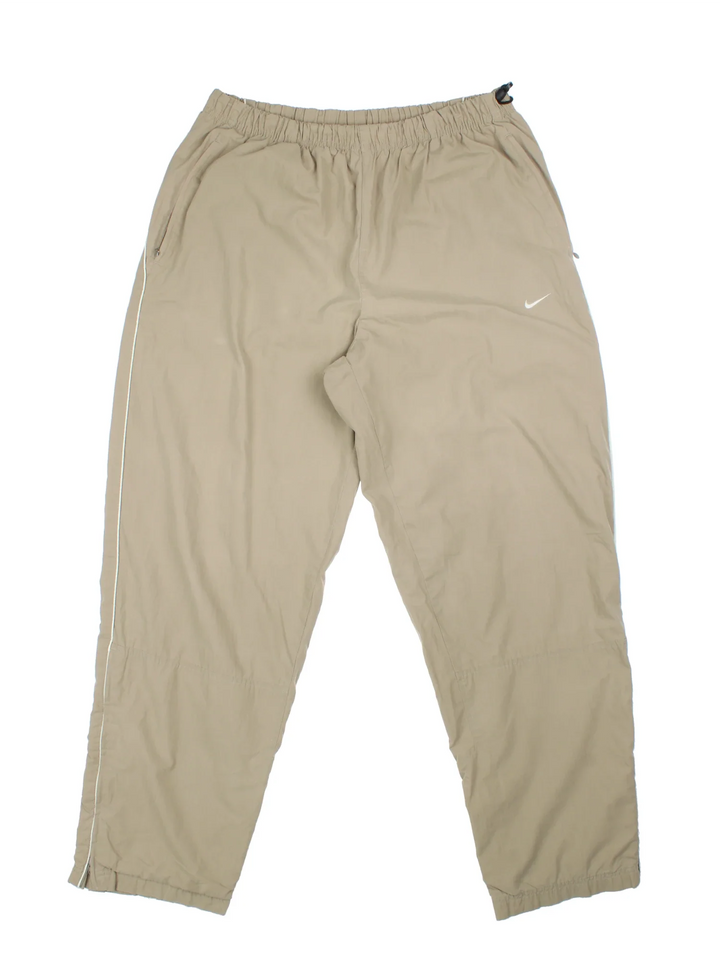 Nike Tracksuit Bottoms in a tan colourway with pockets, elasticated waist, cotton blend lining, and the swoosh logo embroidered on the front.
