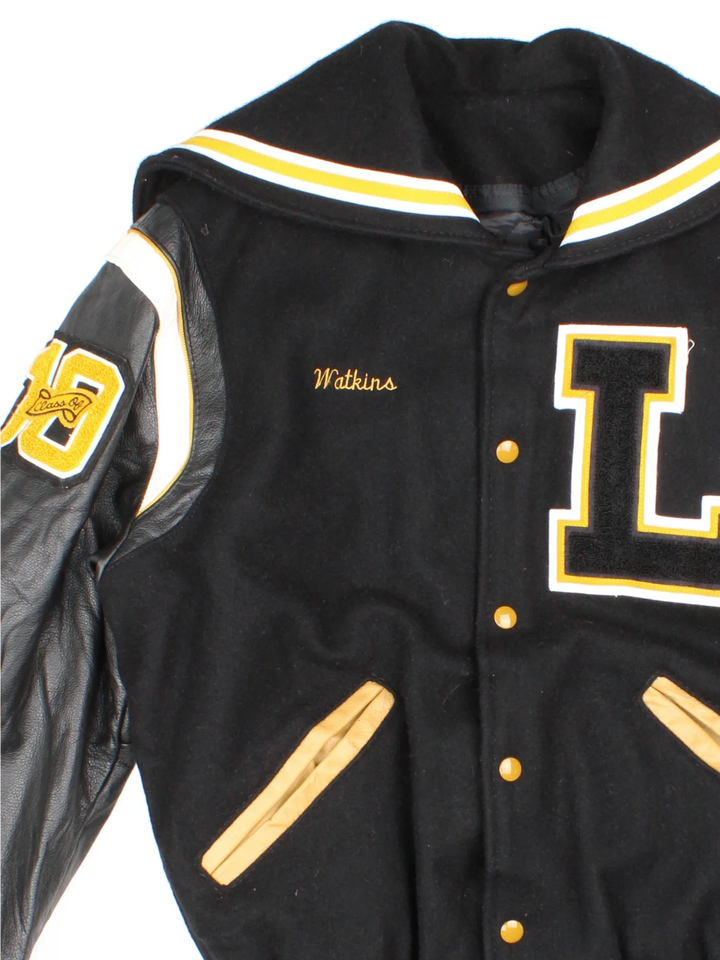 Vintage De Long Varsity Jacket in a black/yellow colourway. Features embroidered badges on front and embroidered spell-out on the back, contrasts cuffs and collars, buttons up and has side pockets. Insulated with a contrast lining.