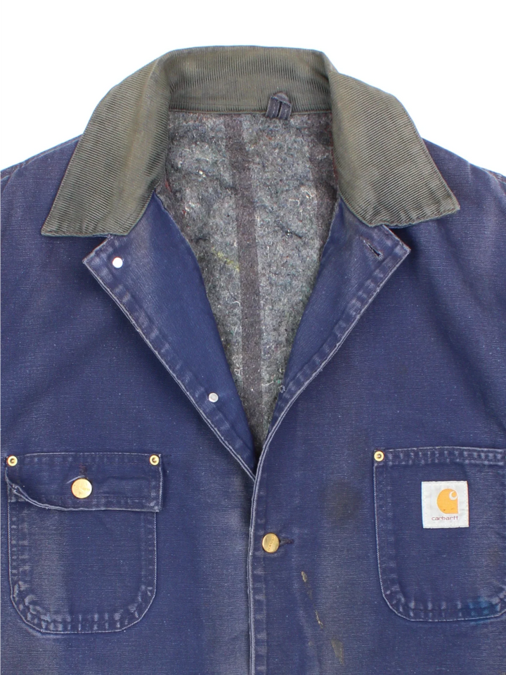 Vintage Carhartt Chore Jacket in a blue colourway with a contrast corduroy collar. Buttons up and has multiple pockets, insulated with a blanket lining, and has the logos embroidered on the front.