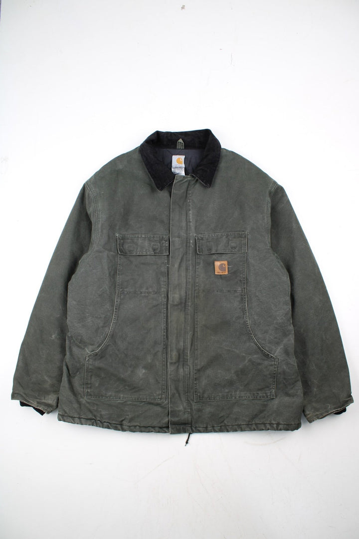 Carhartt Arctic Jacket in a green colourway with a black corduroy collar. Zips up and has multiple pockets, insulated with a quilted lining, and has the logo embroidered on the front.