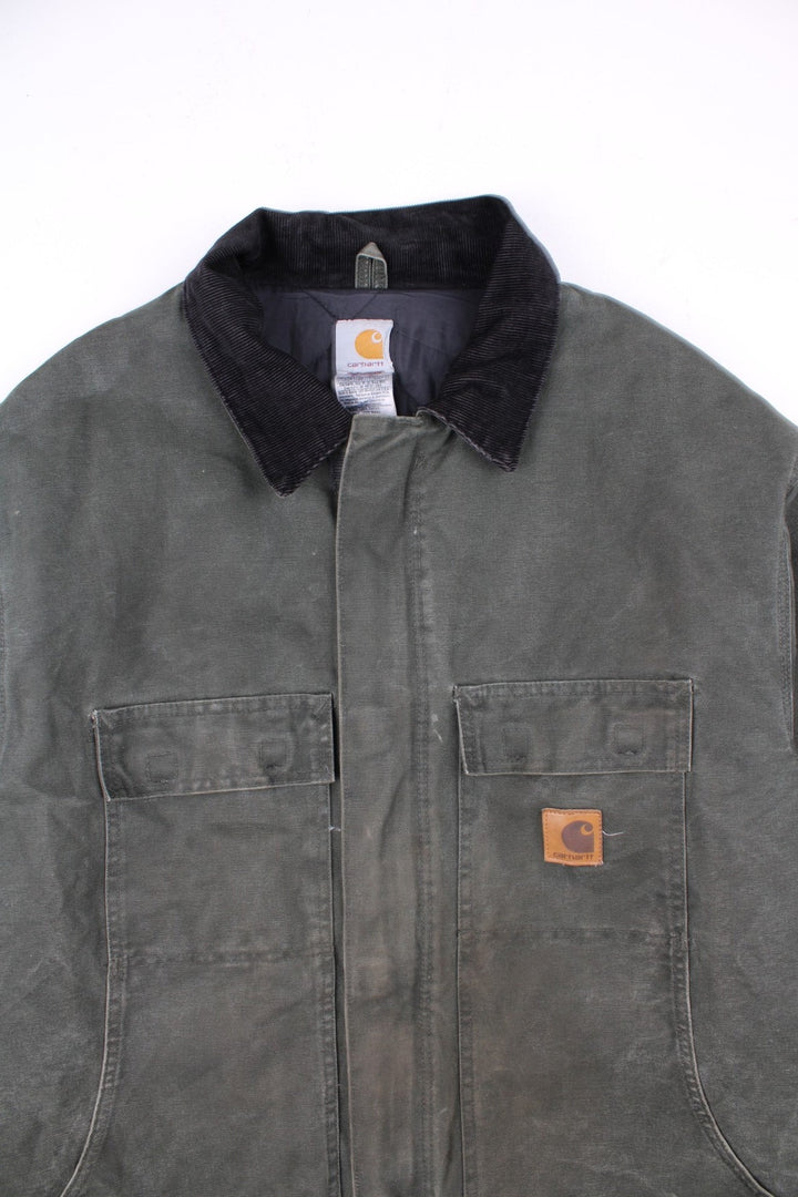 Carhartt Arctic Jacket in a green colourway with a black corduroy collar. Zips up and has multiple pockets, insulated with a quilted lining, and has the logo embroidered on the front.