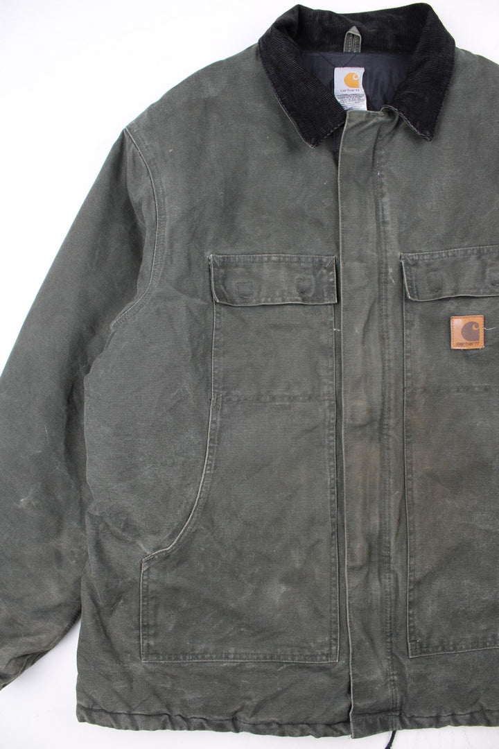 Carhartt Arctic Jacket in a green colourway with a black corduroy collar. Zips up and has multiple pockets, insulated with a quilted lining, and has the logo embroidered on the front.