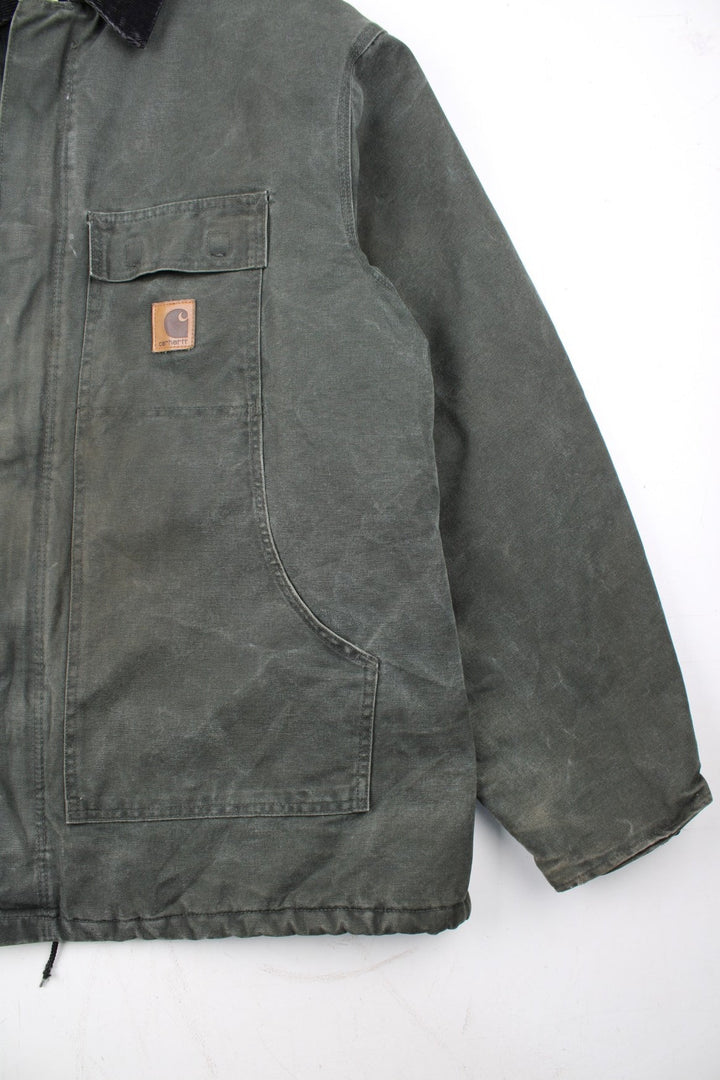 Carhartt Arctic Jacket in a green colourway with a black corduroy collar. Zips up and has multiple pockets, insulated with a quilted lining, and has the logo embroidered on the front.