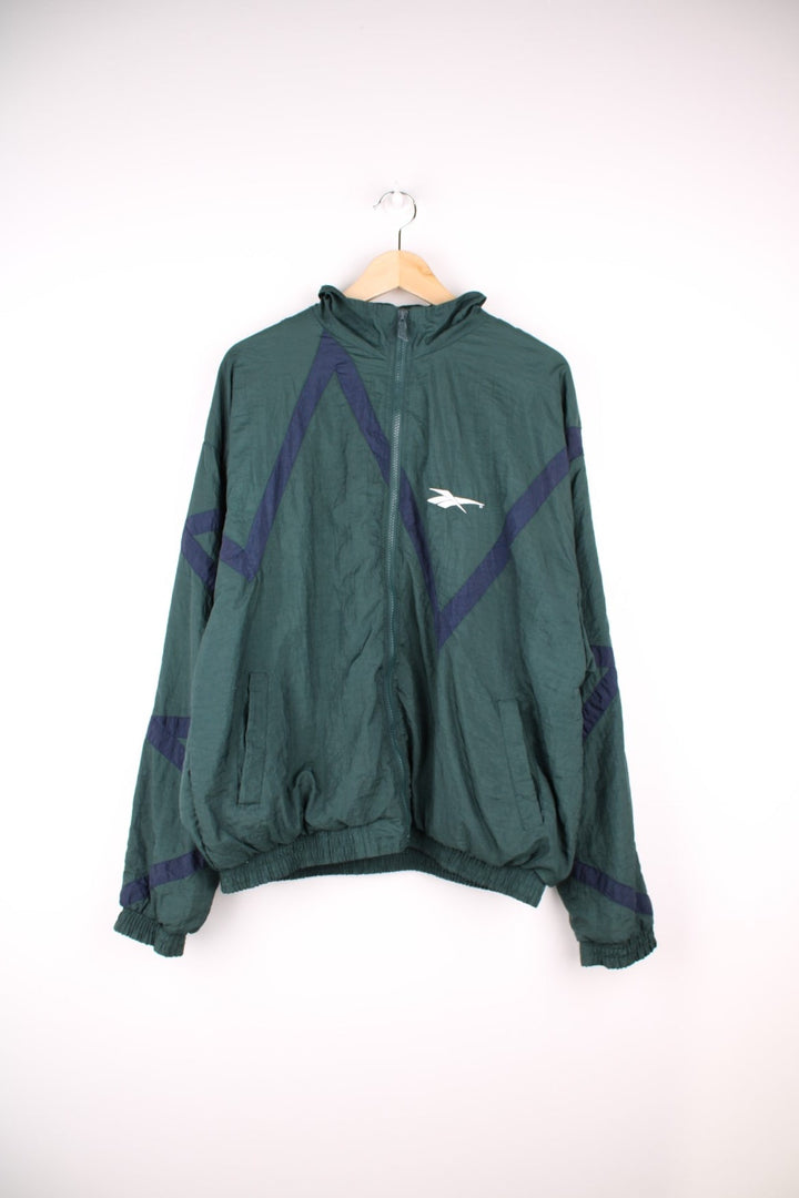 Reebok Tracksuit Jacket in a green colourway with navy blue patterned stripe going across the front and back. Zips up and has side pockets, and the logo is embroidered on the front.