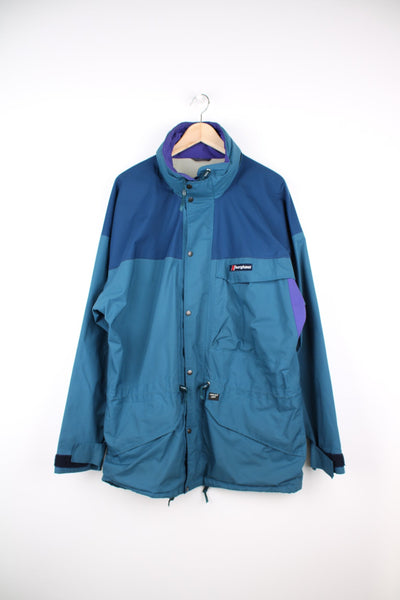 Blue, green and purple Berghaus gore-tex fabric jacket. Features embroidered logo on the chest, drawstring waist and pack away hood.