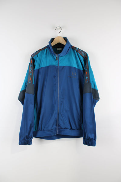 Vintage blue Sergio Tacchini tracksuit top featuring embroidered logo, blue panels and branded stripes down each arm.