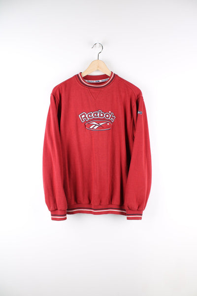 Red Reebok sweatshirt with embroidered logo across the chest and stripe detailing on the neck and cuffs.