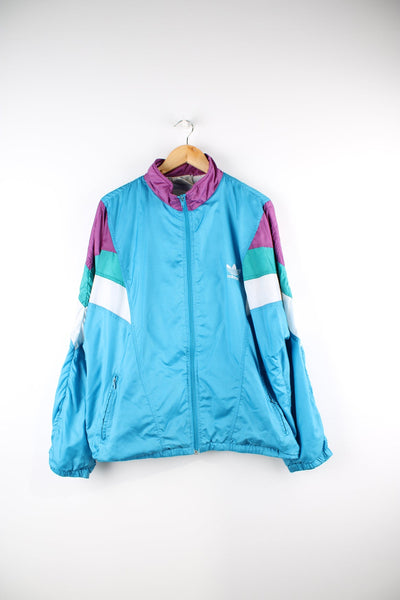 Vintage 90s blue Adidas tracksuit top, features embroidered logo on the chest, as well as a white, green and purple panel feature on both arms.