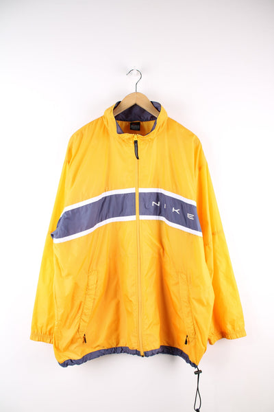 Yellow Nike tracksuit jacket with blue panel across the chest and printed spell out logo.